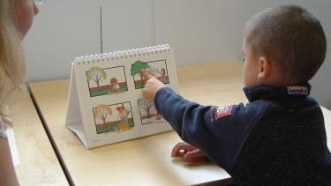 Preschool child dressed in navy blue sweater points at images while a female adult looks on.
