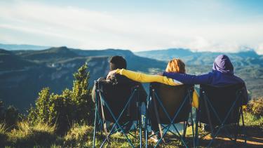 Three young people sit in camping chairs looking out onto a mountain vista